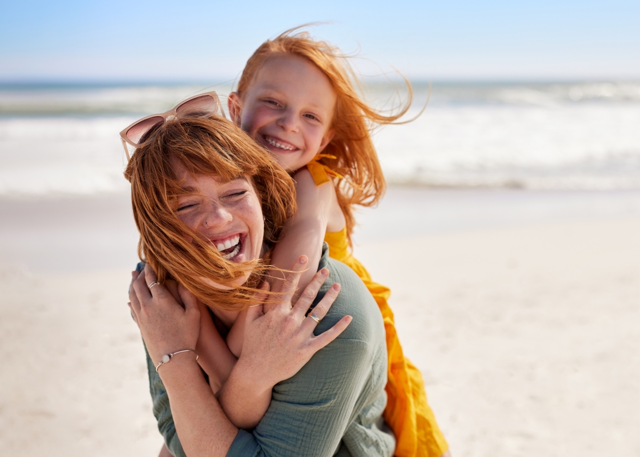 Joyful young mother smiling with little daughter at beach